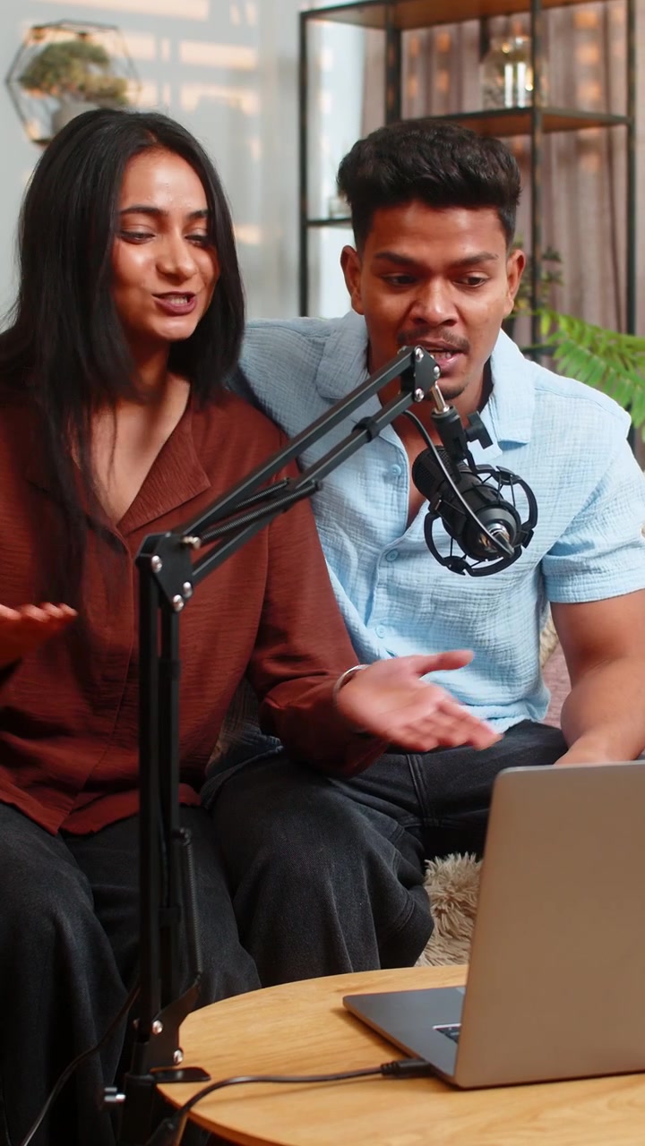 Indisk par, mand og kvinde, sidder i sofaen derhjemme og optager en podcast med mikrofon om familierådgivning