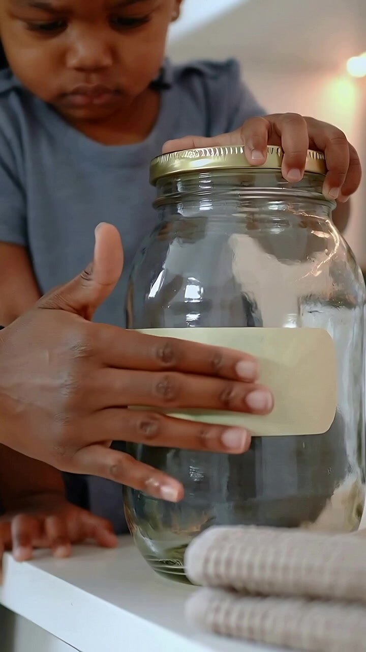 Vertical video: Holding lid toddler grey shirt smoothing label on jar at counter with adult helping