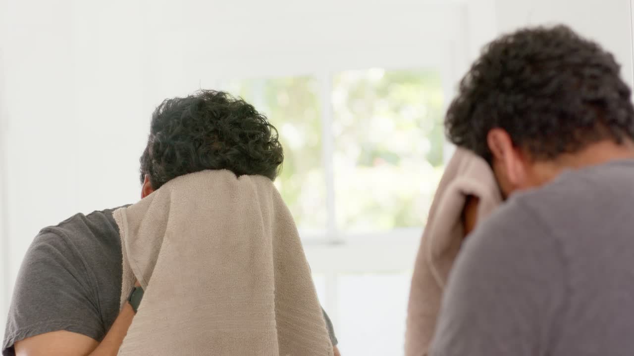 African American man bringing beige towel, drying face and neck, inspecting beard in mirror