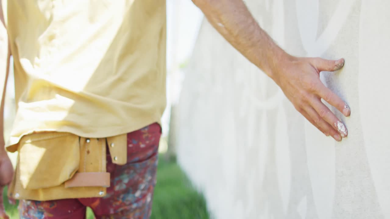 벽에 벽화를 가로질러 손으로 달리는 백인 남성 예술가의 중간 부분의 비디오