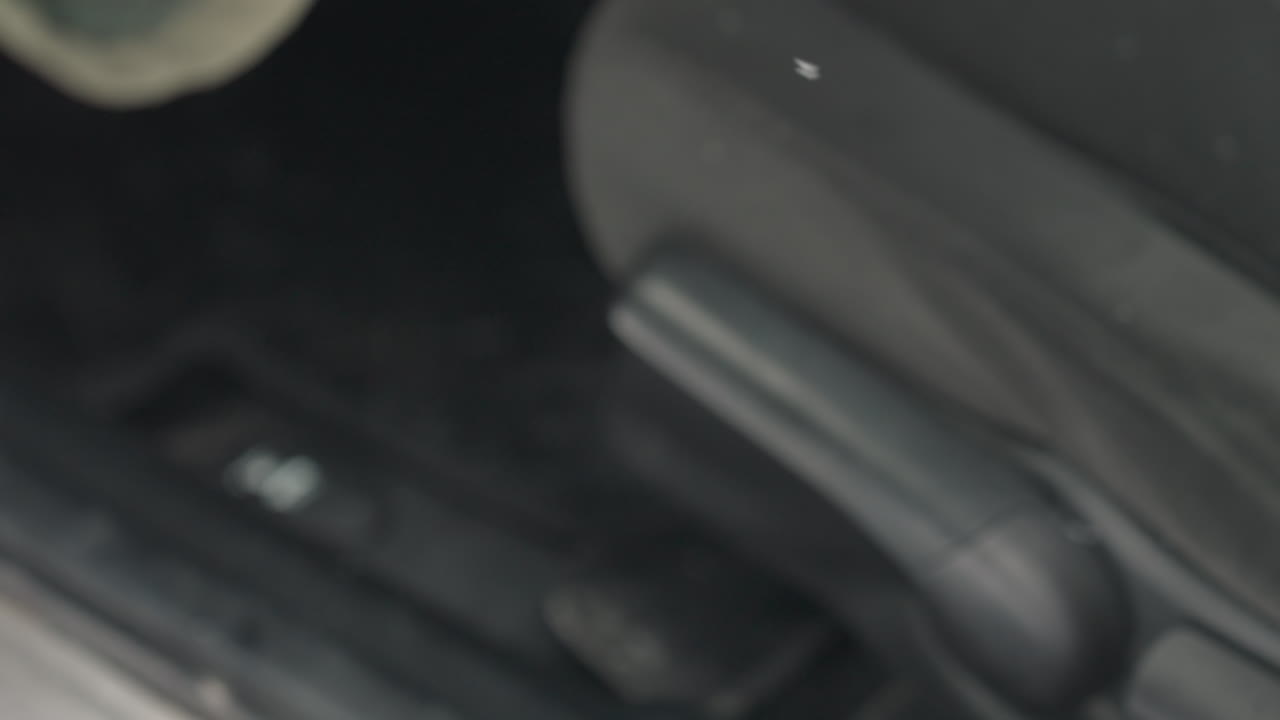 close up of car seat adjustment lever being manipulated by driver hand to reposition fabric seat on metal track against snowy floor mat background