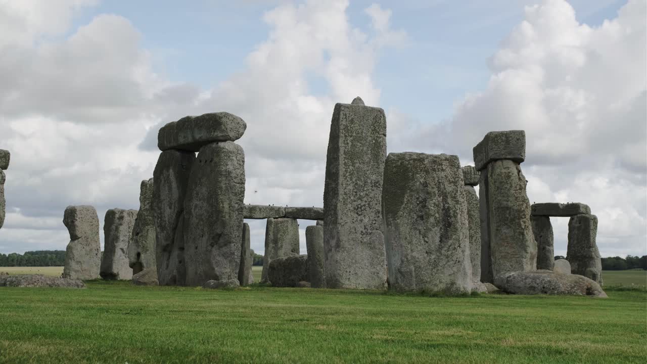 стоунхендж, англия, под голубым небом с белыми облаками и красивыми черными птицами, летающими вокруг скал.