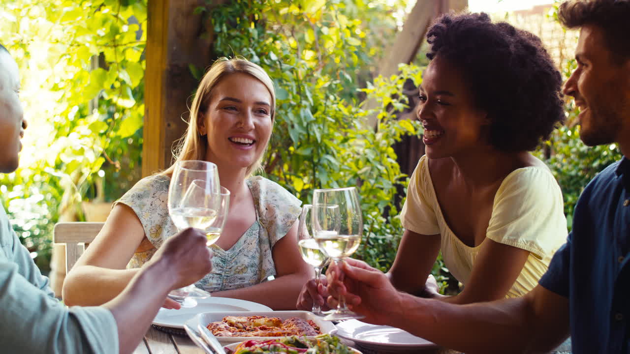 Group Of Smiling Multi-Cultural Friends Outdoors At Home Eating Meal And Drinking Wine Together