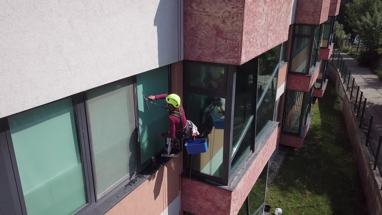 ver hacia abajo al escalador industrial asegurado por cuerdas limpiando las ventanas del edificio de oficinas