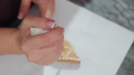 primer plano de una galleta de forma triangular decorada a mano con glaseado blanco de una bolsa de tubería, centrándose en pequeños puntos redondos de glaseado en papel blanco texturizado, con luz natural suave