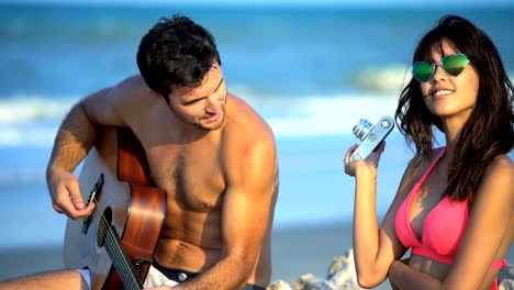 young multi ethnic couple in swimwear playing guitar