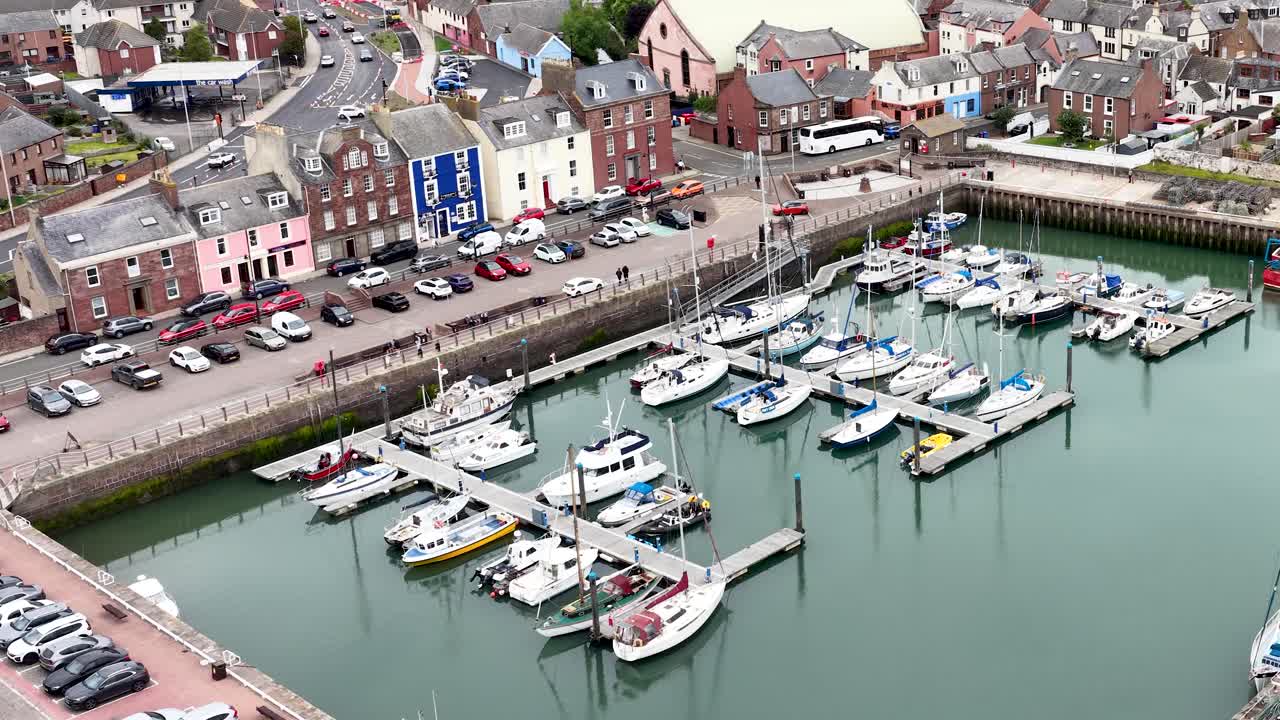 Drone camera moves above marina, boats, and colorful waterfront buildings in overcast daylight