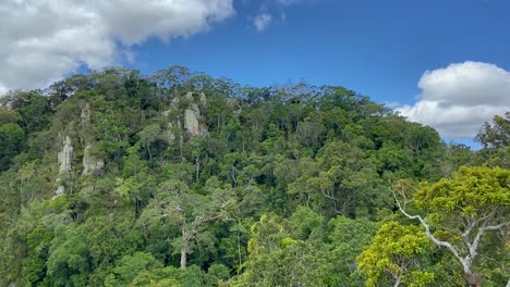 High-aerial-view-flying-over-rocky-escarpments-rising-up-from-the-Amazon-like-rain-forest-jungle,-above-the-dense-green-canopy,-in-tropical-North-Queensland