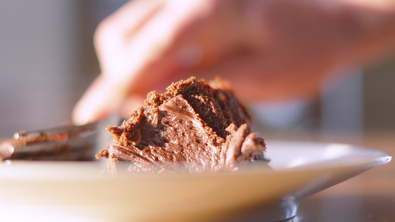Close Up of Fork Cutting Piece of Milk Chocolate Cake Dessert in Sunlight with Shallow DOF Bokeh. Eating Snack Served at Birthday Parties or Afternoon Tea. Food Photography 4K.