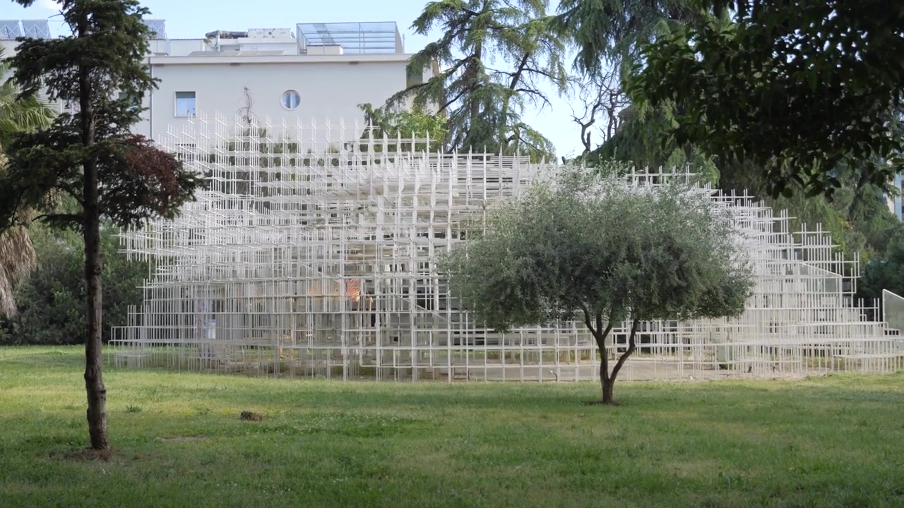 Le pavillon en treillis Reja The Cloud se trouve derrière un petit arbre dans un parc urbain verdoyant à Tirana
