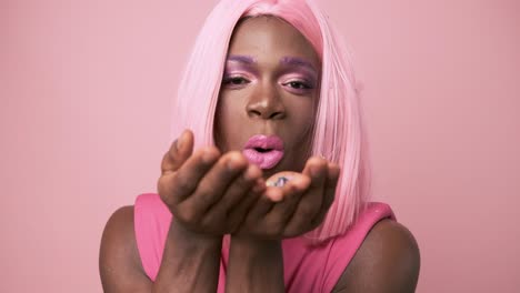 transgender african person with pink dress blowing confetti on pink background