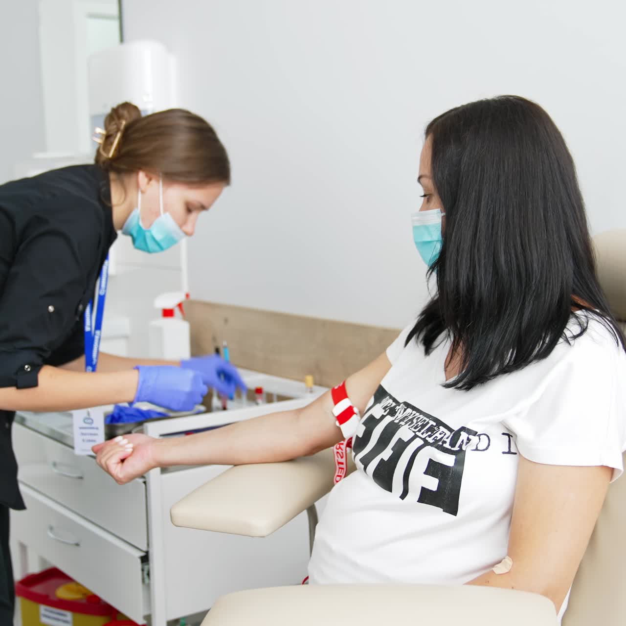 Female nurse taking venous blood from pregnant woman at laboratory. Blood sampling for corona virus antibodies by medical worker indoors. Scientific microbiology test and medical lab equipment