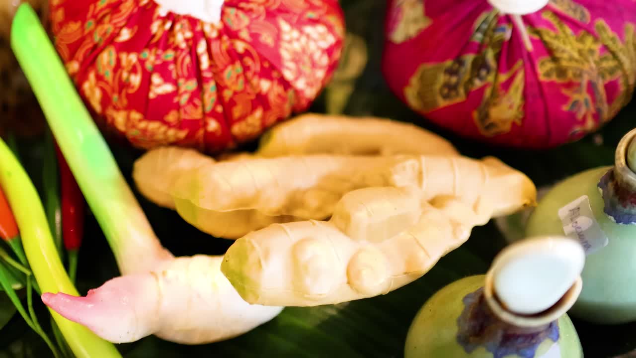 A vibrant arrangement of herbal compresses, ginger, lemongrass, and bottles, showcasing traditional wellness elements.