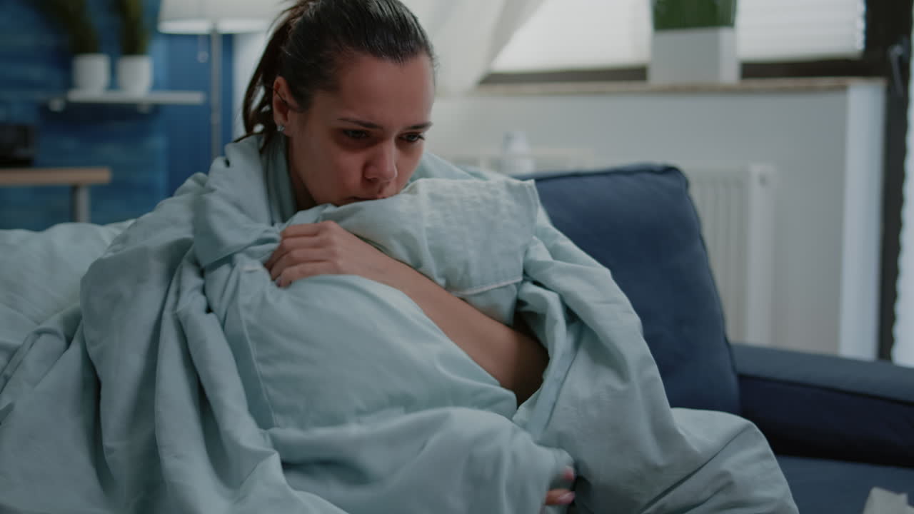 Ill woman with flu using blanket and pillow against shivering