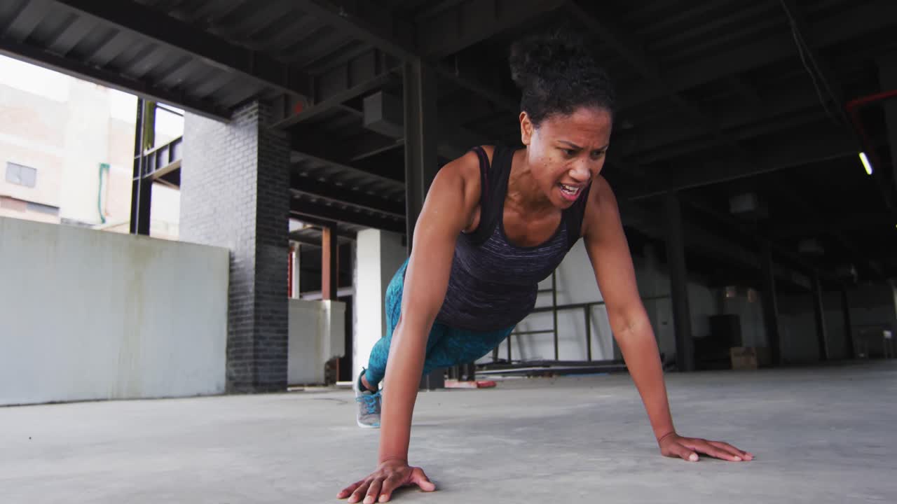 mujer afroamericana haciendo ejercicios de flexión en un edificio urbano vacío