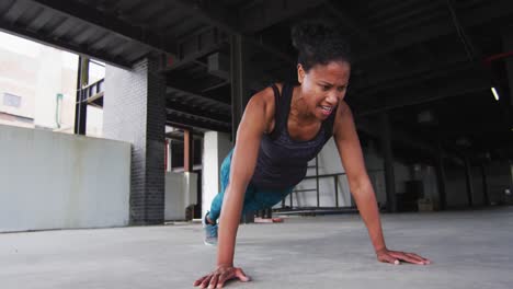 african american woman exercising doing push ups in an empty urban building