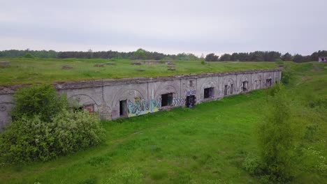 aerial view of abandoned concrete seaside fortification building, southern forts near the beach of baltic sea in liepaja at overcast summer day, wide drone shot moving forward