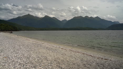 in fiordland, new zealand, a tranquil lake rests amidst lush mountain trees, crafting a breathtaking panoramic vista