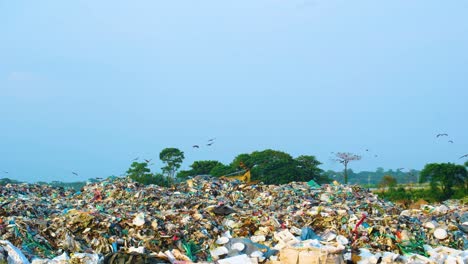 Birds-fly-over-a-vast-waste-landfill-site-located-in-Dhaka,-Bangladesh,-highlighting-issues-of-waste-management-and-environmental-pollution