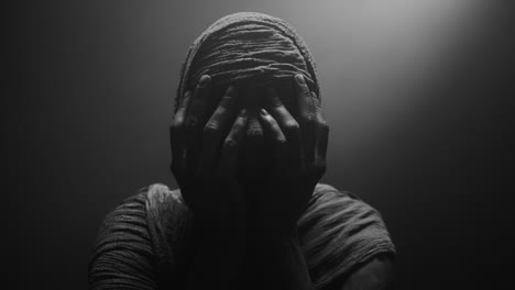 a mummified woman against the dark background in keeps her hands on her face the powerful pose full of despair