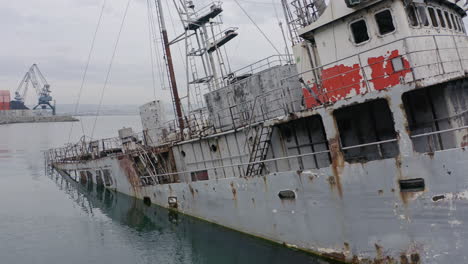 Rusty-grey-half-submerged-shipwreck-anchored-near-the-shore-on-a-cloudy-overcast-day