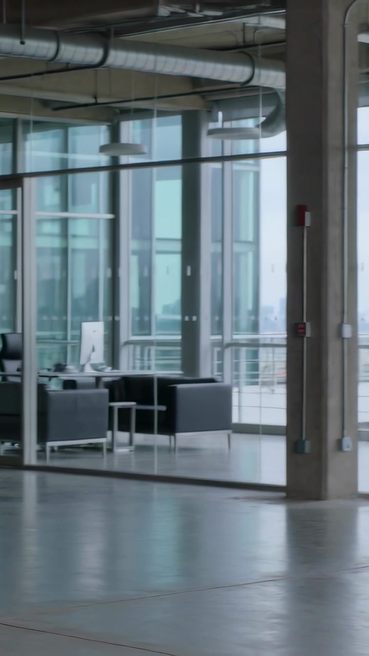 Vertical video: Panning camera revealing glass meeting room in office to show monitor, chair, sofas