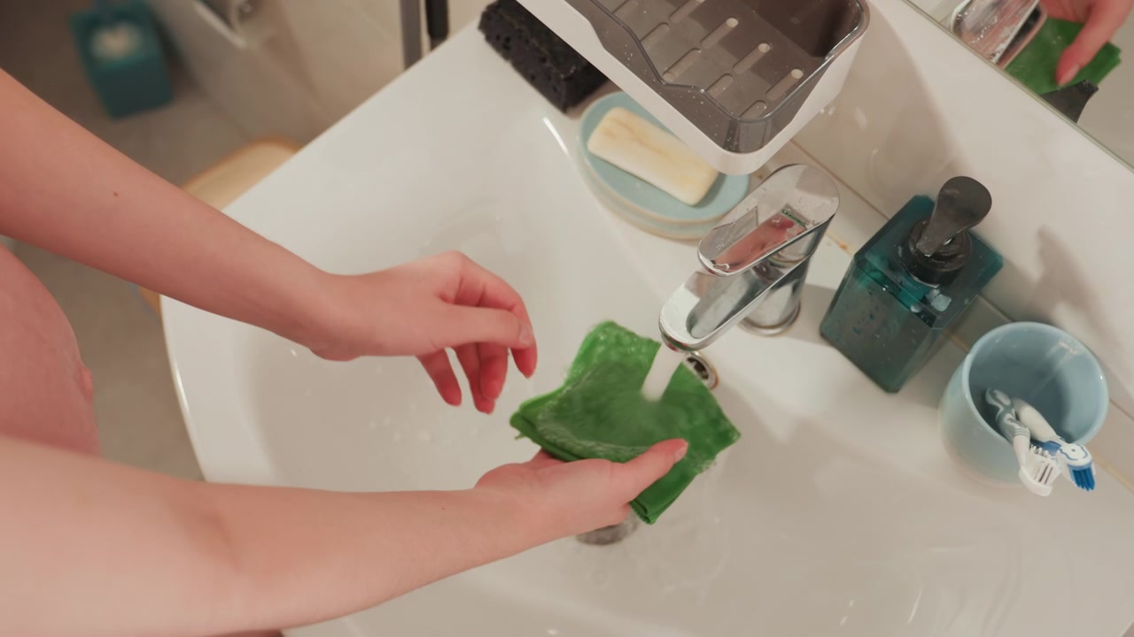 Primo piano di mani che strizzano un panno verde bagnato in un lavandino.