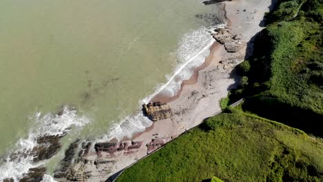 vista aérea de una costa, con una playa de arena vacía y hermosos acantilados
