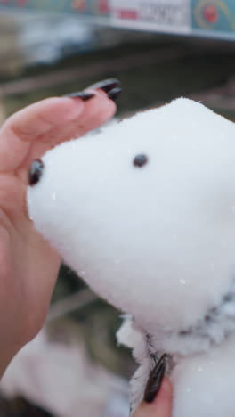 primer plano de una mano con uñas pulidas negras tocando afectuosamente a un oso polar de peluche, enfatizando su textura contra un fondo borroso