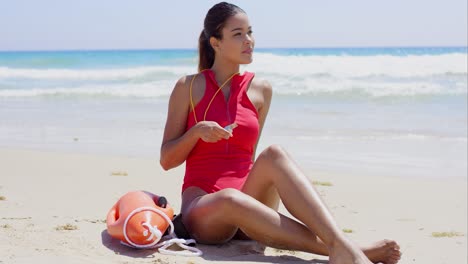 pretty lifeguard sits on beach and twirls whistle