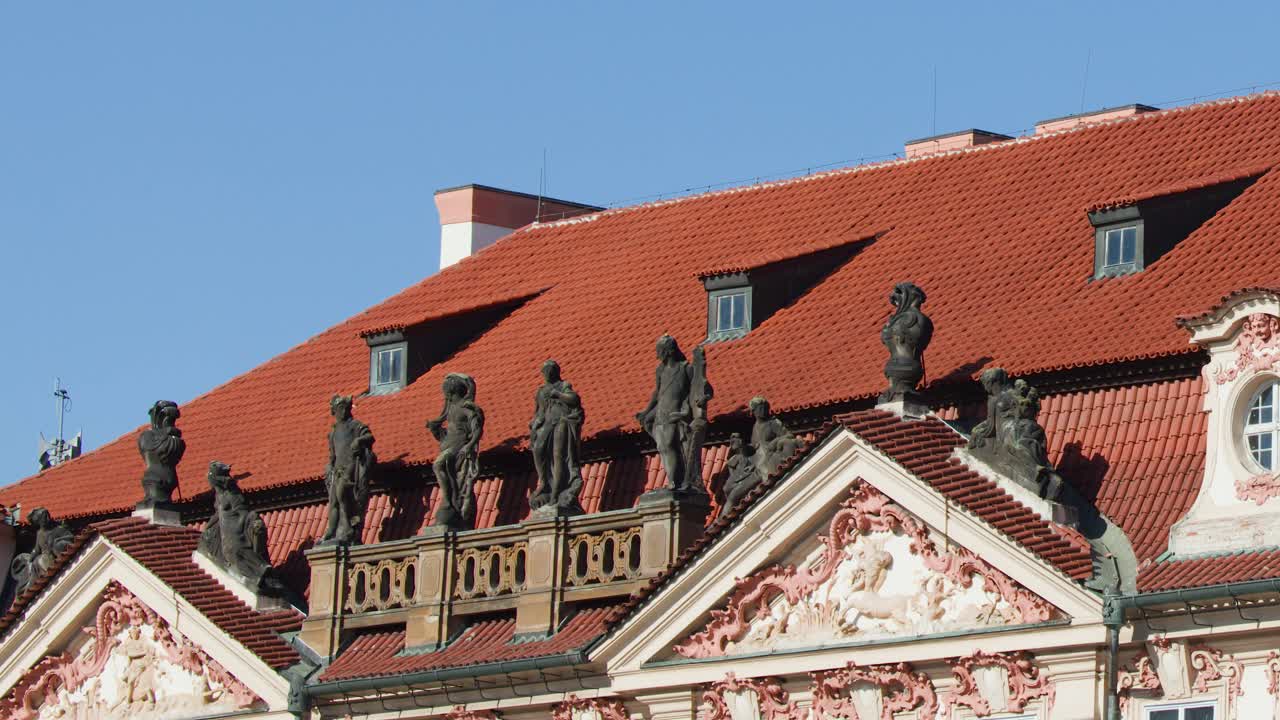 Ornate baroque building rooftop with statues, red tiles, and blue sky in Prague, Czech Republic