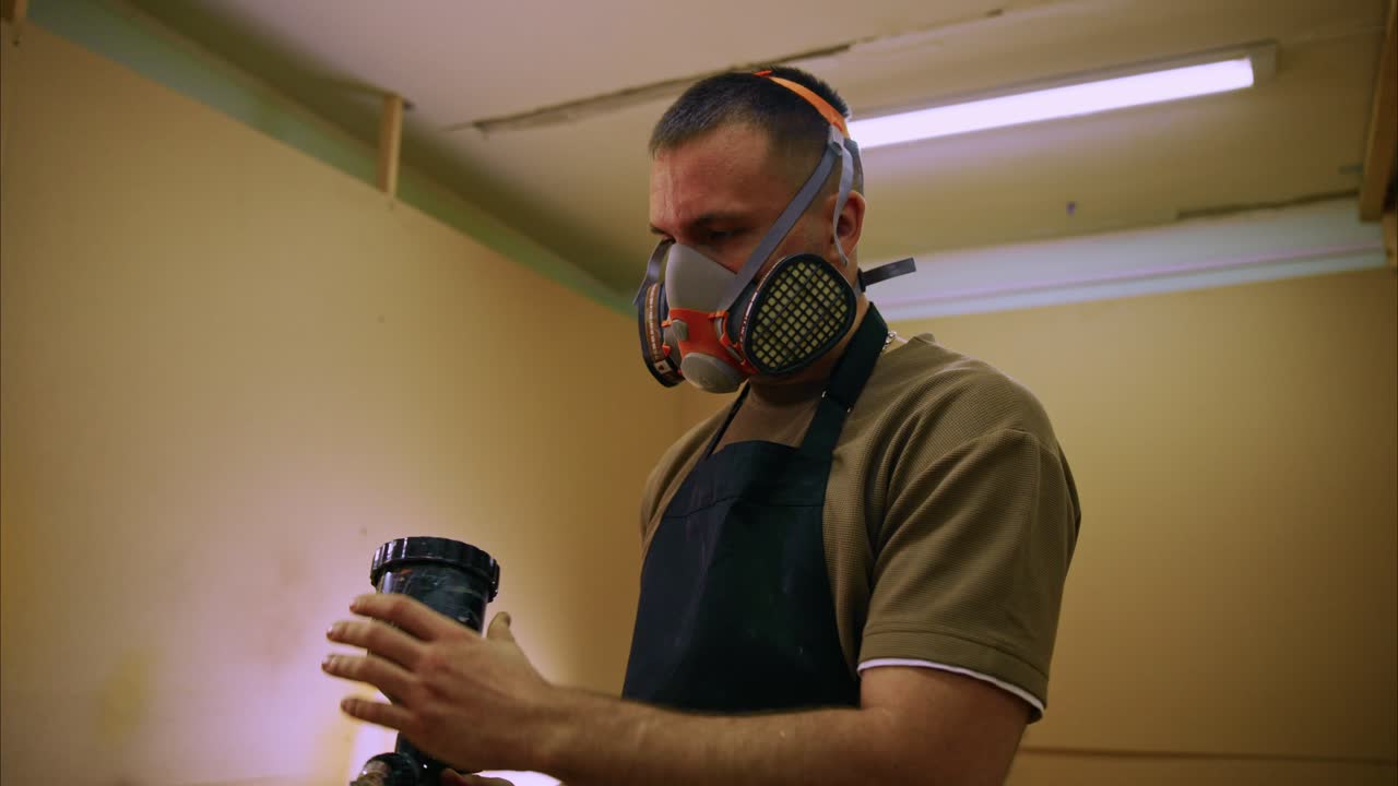 Homem com máscara respiratória preparando pistola de pintura na oficina