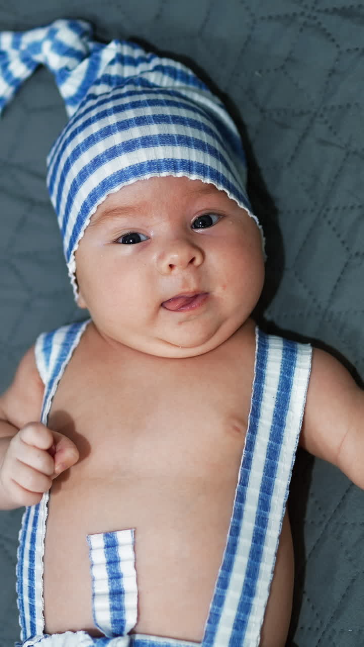 Baby in blue and white striped hat and overalls