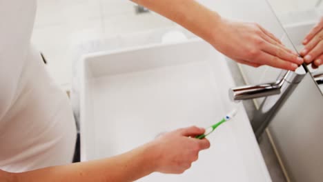 Mujer-Lavando-El-Cepillo-De-Dientes-Debajo-Del-Lavabo-En-El-Baño.