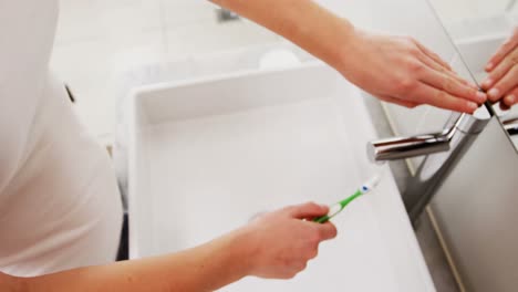 mujer lavando el cepillo de dientes bajo el fregadero en el baño