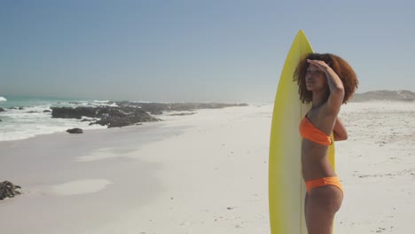 mujer afroamericana mirando la vista del mar con una tabla de surf