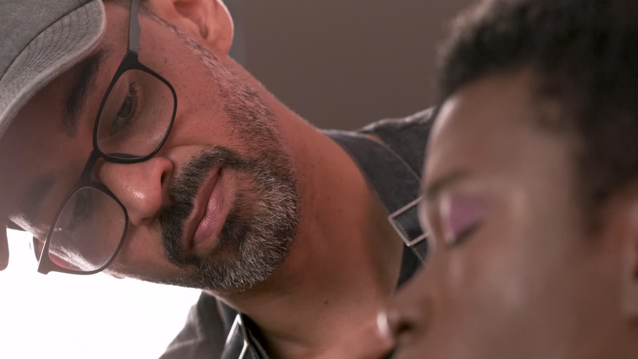 Bearded visagiste applying makeup on drag queen in studio