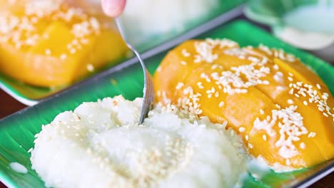 detailed view of mango sticky rice topped with sesame seeds on a green plate.