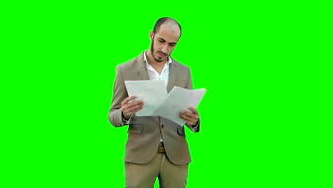 joven hombre de negocios serio de pie y la lectura de algunos documentos en una pantalla verde, clave de croma