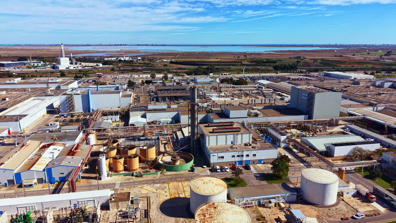Großes Industriegebiet in Wassernähe, mit verschiedenen Gebäuden, Lagertanks und Maschinen unter klarem blauem Himmel