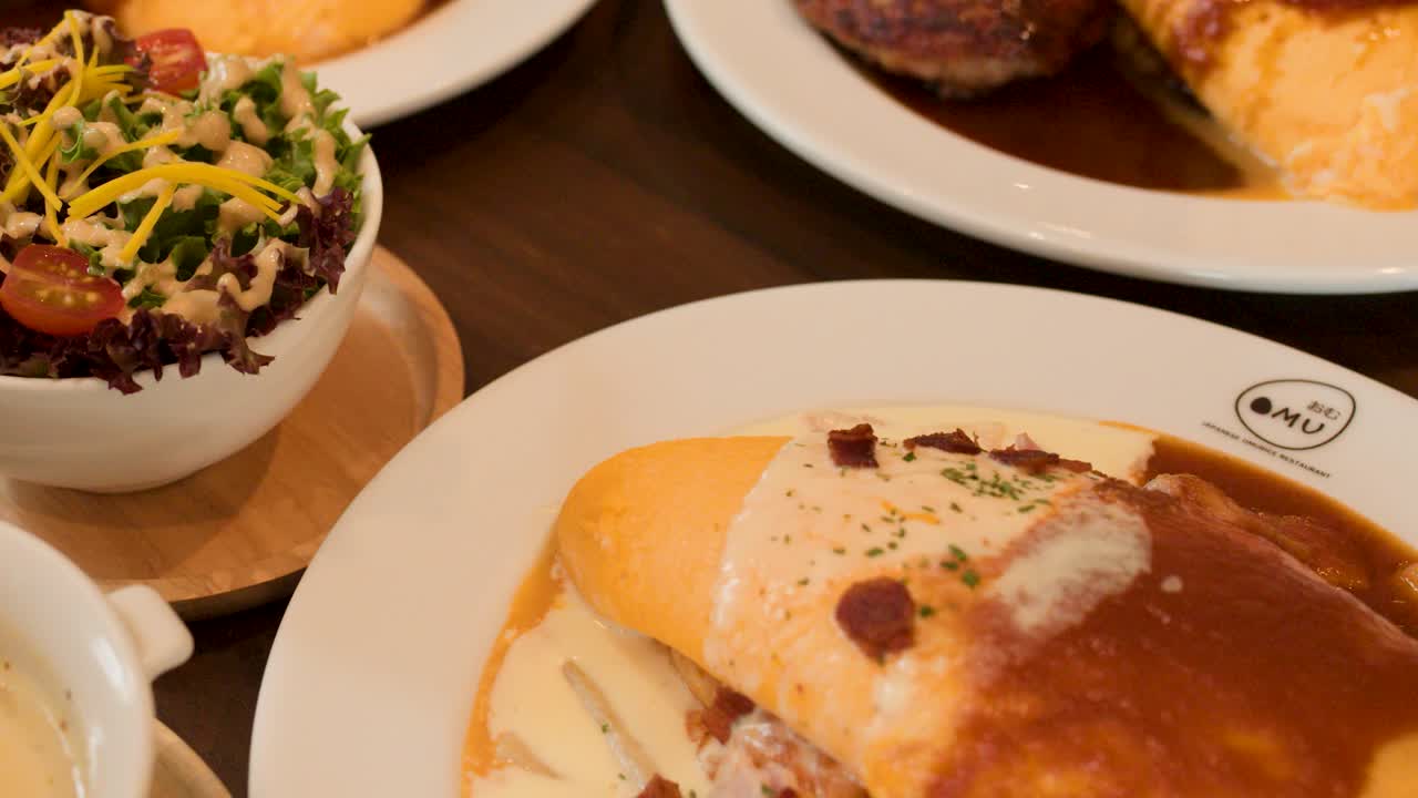 Close-up of Japanese omelette rice, creamy soup, and salad in warm restaurant lighting