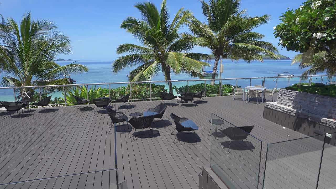 Wide open patio view with dark wicker chairs, palm trees, and blue ocean background at Sheraton Tokoriki