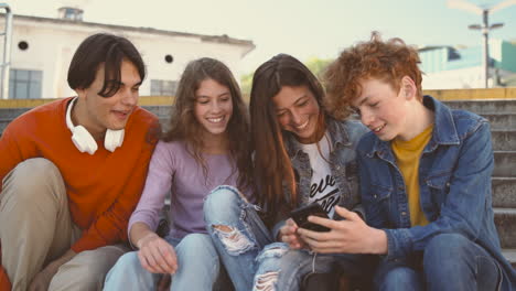 un grupo de adolescentes con dos chicas y dos chicos viendo algo divertido en un teléfono celular 2