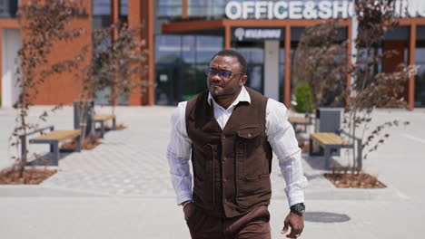 handsome afro american businessman walks outdoors. portrait of confident dark skinned man with sportive body walking step by step in the city. slow motion.