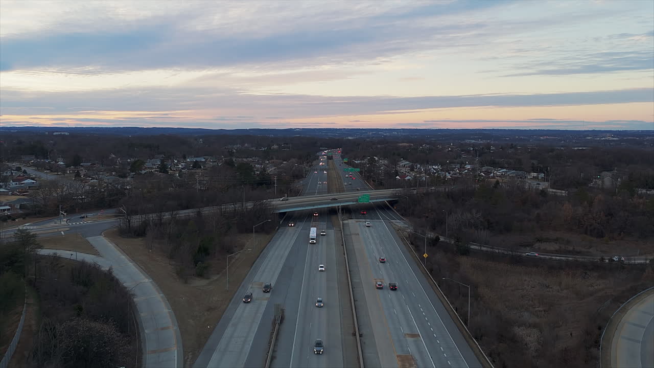 Aerial View Of US Highway At Dusk, With Light Traffic And Exit Ramps. Suburban Neighborhood In Background.