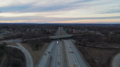 aerial view of us highway at dusk, with light traffic and exit ramps. suburban neighborhood in background.
