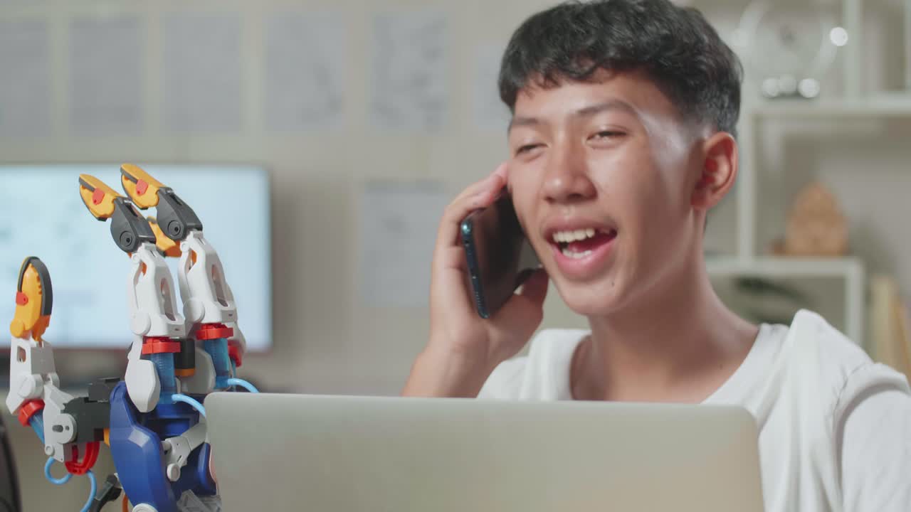 집에서 노트북을 사용하는 사이보그에 대해 작업하는 동안 스마트폰으로 이야기하는 아시아 소년의 클로즈업