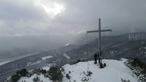 Cruz-De-La-Cumbre-En-Invierno-Con-Dos-Excursionistas-En-La-Parte-Superior