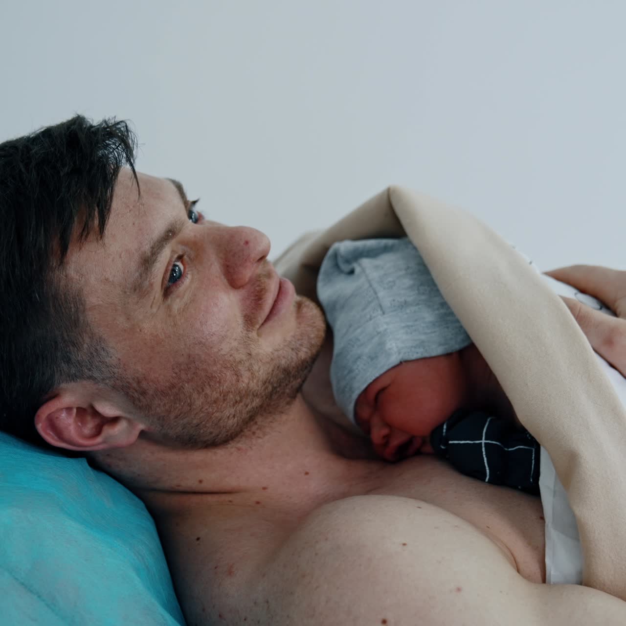Caucasian father holding his newborn baby on the bare chest. Little child cries bitterly. Infant born through C-section