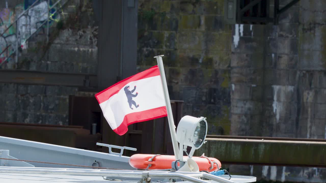 Berlin city flag flutters on boat stern, river harbor background, daylight, stable camera, close-up